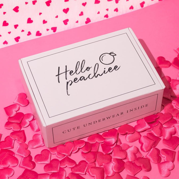 Hello Peachiee branded shipping box with heart confetti on pink background